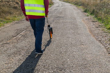 Surveyor measuring road distance with odometer wheel on asphalt country road