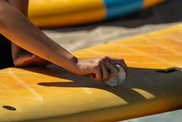 Surfboard wax. Hand holds a piece of surf wax and lubricates the surfboard. Waxing a surfboard.