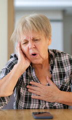 Senior woman with a pained expression, clutching her chest and holding her face, showing clear signs of distress or discomfort.