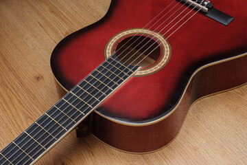 Fototapeta premium A red guitar with a black fretboard sits on a wooden surface. The guitar is a vintage model and has a black and gold design. The wood grain of the surface adds to the overall aesthetic of the image.