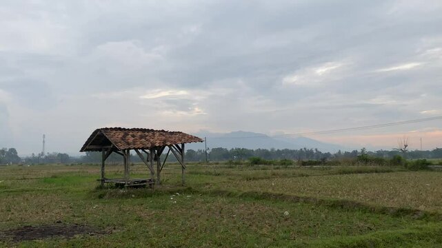 small wooden hut  is situated in a field of  grass , with  a cloudy sky overhead 