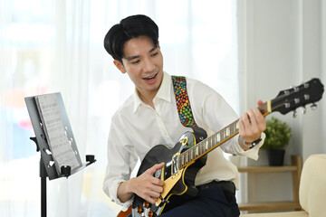 Handsome male guitar player practicing at home with music stand