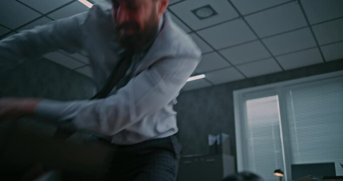 Aggressive businessman loses his temper in a fit of rage. Furious male office employee smashes computer monitor with keyboard, throws things off the desktop and yells. Financial crisis or dismissal.
