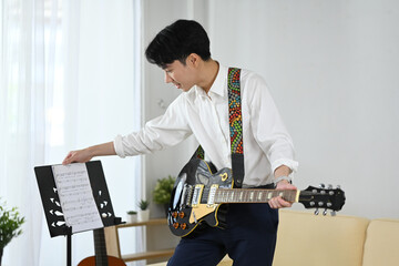Handsome male guitar player practicing at home with music stand