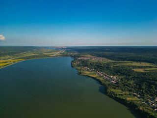 Panorama with a storage dam captur with a drone in the countryside. A calm river that comes from the mountains among the green forests and flows into the lake at the edge of a village in Romania