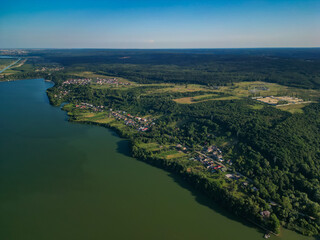 Fototapeta premium Panorama with a storage dam captur with a drone in the countryside. A calm river that comes from the mountains among the green forests and flows into the lake at the edge of a village in Romania