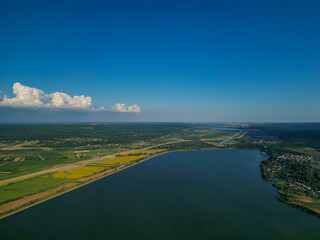 Panorama with a storage dam captur with a drone in the countryside. A calm river that comes from the mountains among the green forests and flows into the lake at the edge of a village in Romania