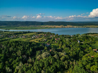 Fototapeta premium Panorama with a storage dam captur with a drone in the countryside. A calm river that comes from the mountains among the green forests and flows into the lake at the edge of a village in Romania