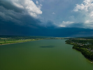Panorama with a storage dam captur with a drone in the countryside. A calm river that comes from the mountains among the green forests and flows into the lake at the edge of a village in Romania