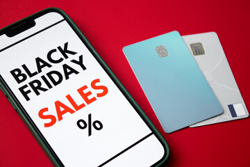 Close up of a smartphone screen displaying a Black Friday online sale on red background with credit cards and money