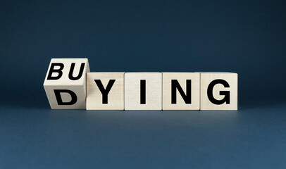 Blocks spell out BUYING with the first block tilted to reveal DYING