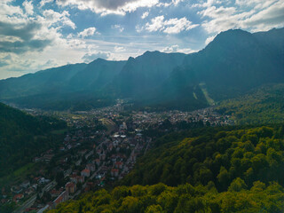 Fototapeta premium A town at the base of the mountain in the autumn season. Astonishing aerial view with the rocky mountains filmed in cinematic style. Romanian landscape above Busteni city in a sunny day with blue sky