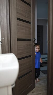 Door opens and a cute little boy appears. Caucasian child enters the bathroom at home. Vertical video.