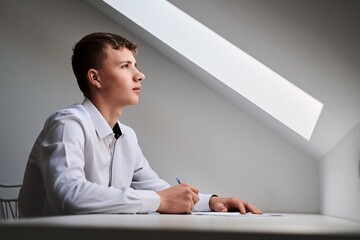 Portrait of a high school student in a white uniform doing homework, sitting at a table with...