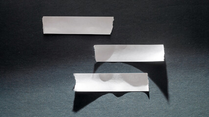 Three torn strips of white paper are arranged unevenly on a dark background, creating copy space.