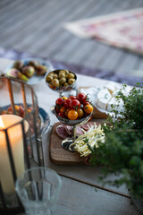Beautiful autumn table setting: cheese, prunes, tomatoes, salami, olives, figs on the wooden table, decorated with potted thyme, candles, close up view 