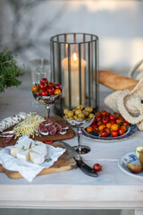 Beautiful autumn table setting: cheese, prunes, tomatoes, salami, olives, figs on the wooden table, decorated with potted thyme, candles, close up view 