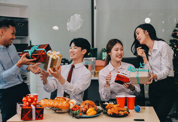 full length view of a group of business team wearing red Santa hat and exchange gift box together in the office for Christmas.