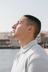 Portrait of a young arab male captured outdoors with his eyes closed. Generation Z man standing near waterfront in Old Town, Dubai