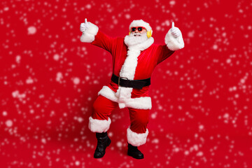 Full body size photo of pensioner old man grey beard show thumbs up party dancing wear santa x-mas costume coat sunglass headwear wireless earphones boots isolated red color background