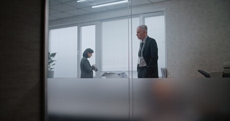 Fototapeta premium Office robbery case: Crime investigation team at crime scene. Female criminalist takes photos of clues and evidence, then talks to male detective. African American policeman searches fingerprints.