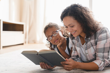 African mother mom reading fairy tales book novel with daughter girl, learning together, helping...