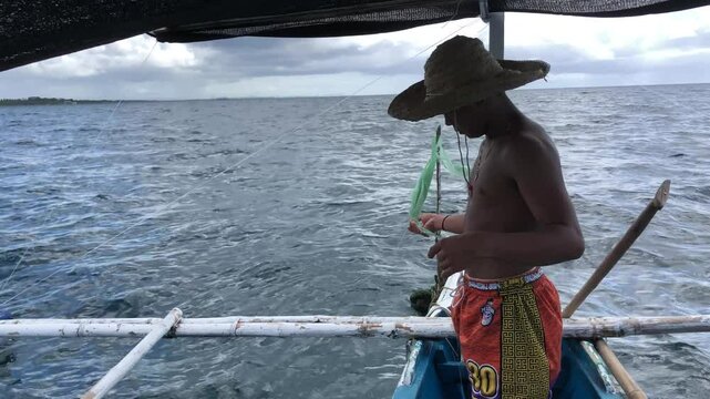 young man is fishing with a handline from a boat in deep sea waters.