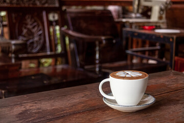 Fototapeta premium Cappuccino in a White Cup with some Wooden Furniture in the Background
