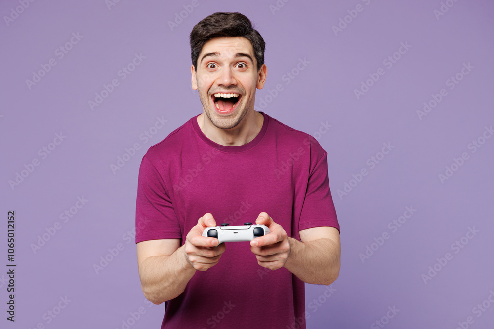 Poster Young surprised Caucasian man he wear violet t-shirt casual clothes hold in hand play pc game with joystick console isolated on plain pastel light purple background studio portrait. Lifestyle concept.