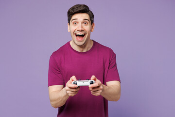 Young surprised Caucasian man he wear violet t-shirt casual clothes hold in hand play pc game with...