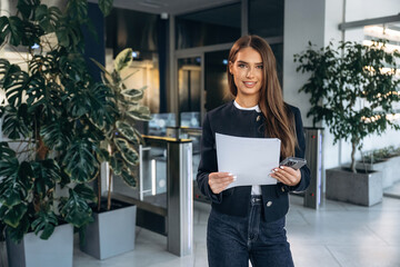 Front view, holding document. Woman is indoors, professional manager of the place