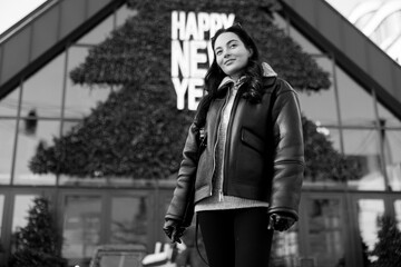 Young pretty woman standing on city street against background of decorated Christmas tree and building.