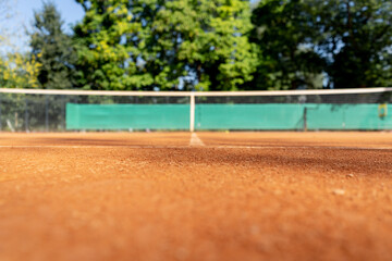 low shot close-up professional tennis field with stretched net field markings clay surface green trees early morning