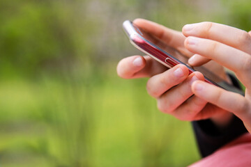 Closeup of a hand holding a mobile phone an outdoor setting. Teenager girl using smartphone, texting or browsing. Mobile technology in daily life. Modern lifestyle. Selective focus. Copy space
