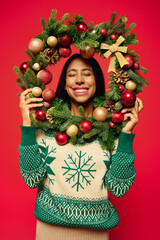 A joyful young woman holds a colorful Christmas wreath full of ornaments.