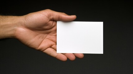 Obraz premium Hand holding a blank card on a dark background, ready for customization or message.