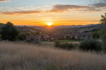 The image presents rolling hills and expansive fields under a vividly colored sunset sky, creating a stunningly serene and picturesque rural landscape scene.