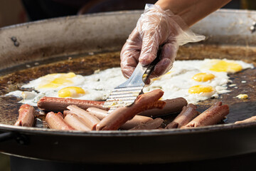 A person is cooking hot dogs and eggs on a grill