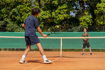professional tennis court young curly guy playing tennis with blond opponent pair training active rest practicing serve with racket