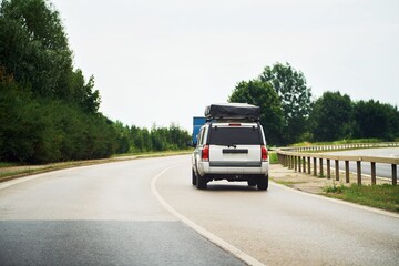 Car with rooftop cargo box and sleeping tent on road