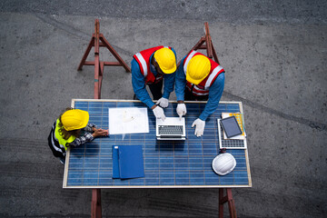 Three men are working on a solar panel project. They are wearing safety gear and are looking at a laptop