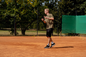 on professional tennis court a young blond guy practices hitting a tennis ball practice of a low kick