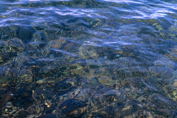 Underwater pebble backgrounds. Colorful stones sea bottom in the sun rays. View from above through clear water. Seascape wallpaper texture. Defocus.