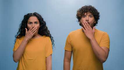 Multiracial shocked scared afraid couple amazed shocked Hispanic woman hiding behind Indian man...