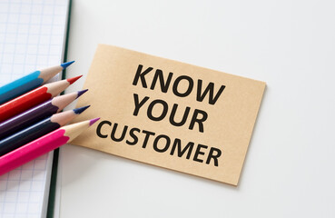 Text Know Your Customer on beige sticker with colored pencils and notebook on white table