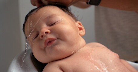 baby having water poured over head during bath, baby relaxed and calm while water flows, wet hair,...