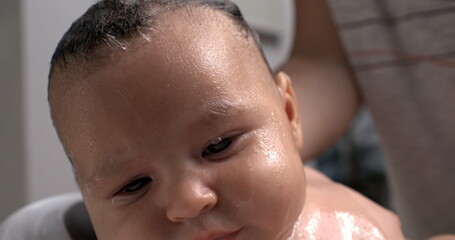 Hand gently covering baby’s head while washing during bath, protective gesture, baby calm and...