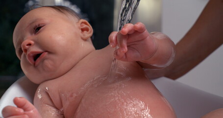 Water pouring over baby’s chest during bath, baby tilting head and looking calm, relaxing bath...