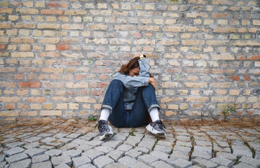 Stressed female curling up, sitting on the ground hiding her face with her hands. Deep emotional...