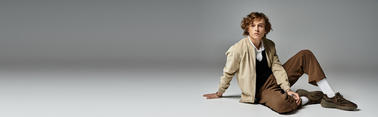 A stylish young man with wavy hair showcases his autumn outfit in a chic studio setting.